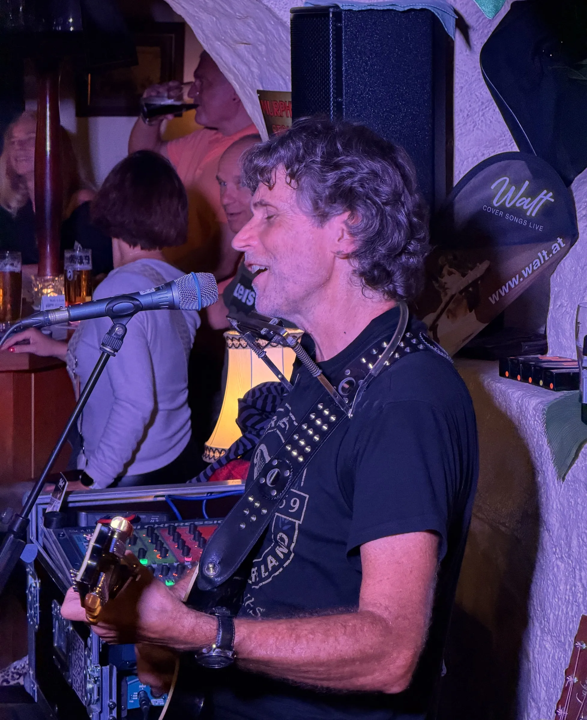Walt singt mit Gitarre und Harp, vor ihm das Digitalmischpult im Rack, hinter ihm Lautsprecher und Walt-Banner